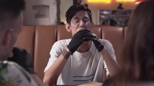 Lindo joven flaco en gafas y guantes negros comiendo sabroso shawarma. El hombre que disfruta de la deliciosa comida rápida en el restaurante moderno . — Vídeos de Stock