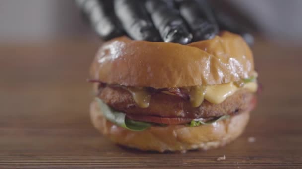 黒いゴム手袋をしたシェフの手がハンバーガーとソースを押し出し、クローズアップで流れ出します。おいしい食べ物の準備。テーブルの上にジューシーな食欲ハンバーガー。スローモーション. — ストック動画
