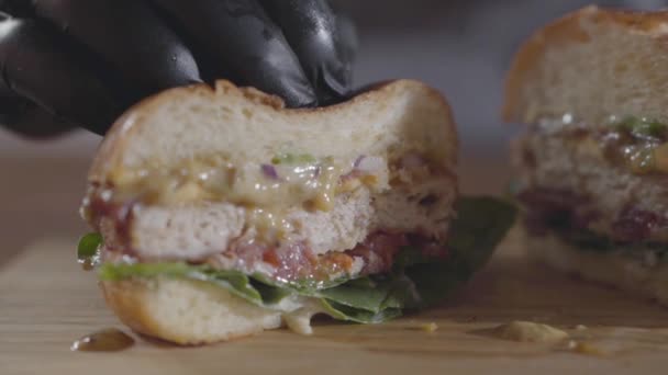 Primeros planos de las manos del chef en guantes de goma negro presionando mitades de hamburguesa y salsa que fluye hacia fuera. Sabrosa preparación de alimentos. Hamburguesa jugosa y deliciosa sobre la mesa. Movimiento lento . — Vídeo de stock