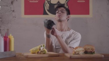 Sakallı adam ağız sulandıran burger ve shawarma yemek için hazırlanıyor önünde masada oturuyor. Siyah eldiven giyen adam..
