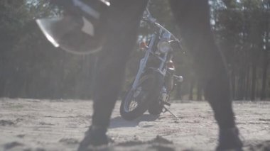Yumuşak ışıkta çam ormanı önünde kum üzerinde motosiklet ayakta kızın bacakları. Hobi, seyahat ve aktif yaşam tarzı. Kadın bisikletçi motosikletaçık