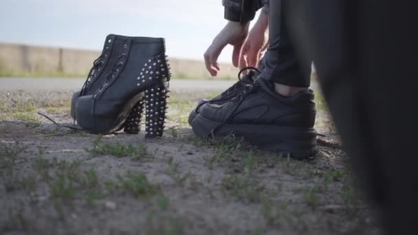 La giovane donna cambiando le sue scarpe moto su scarpe a spillo con tacchi alti primo piano. Brutalità e concetto di femminilità. Tempo libero e viaggi in moto . — Video Stock