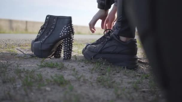 A jovem mulher trocando seus sapatos de moto em sapatos cravados com salto alto close-up. Brutalidade e conceito de feminilidade. Lazer e viagens de moto . — Vídeo de Stock