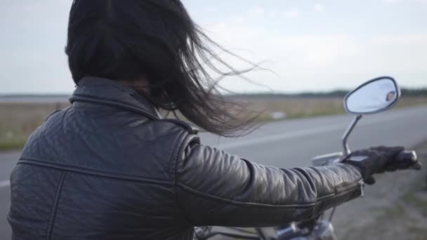 Achteraanzicht van onherkenbaar meisje in oude leren jas zittend op de motorfiets kijken weg. Hobby, reizen en actieve levensstijl. Vrouwelijke Biker buitenshuis. Vrije tijd en reizen met de motor — Stockvideo