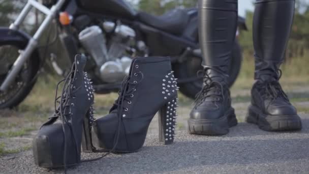 La giovane donna cambiando le sue scarpe moto su scarpe a spillo con tacchi alti primo piano. Brutalità e concetto di femminilità. Tempo libero e viaggi in moto . — Video Stock