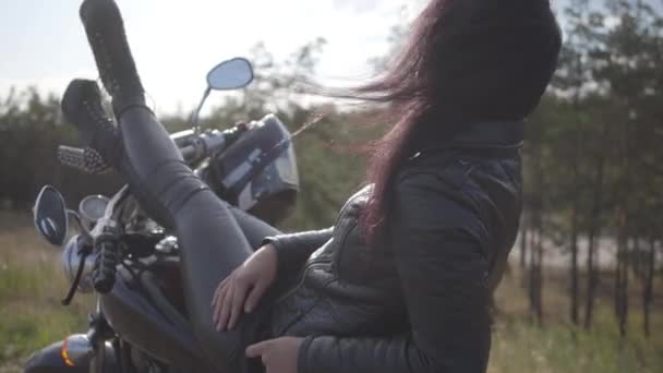 Pretty young caucasian woman in a black leather jacket and pants lying on a classic motorcycle. Hobby, traveling and active lifestyle. Leisure and travel by motorbike. — Stock Video