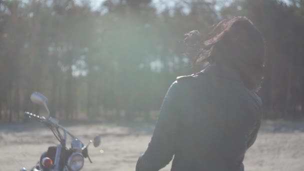 Vista trasera de la joven mujer que se pone el casco de la motocicleta de pie en su nueva moto en luz suave. Hobby, viajar y estilo de vida activo. Motociclista al aire libre montando una moto — Vídeo de stock