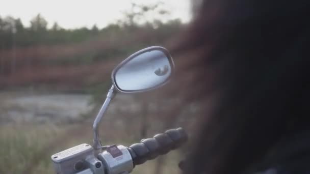 Achteraanzicht van onherkenbaar meisje zittend op de motorfiets schoonmaken van de spiegel met haar gehandschoende hand. Haar fladderende in de wind. Hobby, reizen en actieve levensstijl. Vrouwelijke Biker buitenshuis — Stockvideo