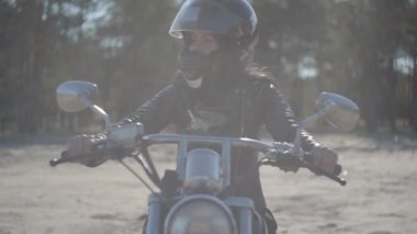 Portre sevimli kız siyah kask giyen motosiklet üzerinde oturan uzağa bakıyor. Hobi, seyahat ve aktif yaşam tarzı. Bisikletçi dışarıda motosikletine biner. Eğlence ve motosiklet ile seyahat. Yumuşak ışık.