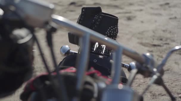 Zapatos de punto con tacones altos y vestido negro y rojo acostado en el primer plano de la motocicleta. La moto con el casco en la rueda en la orilla del río. Aficion, viajes y estilo de vida activo — Vídeos de Stock