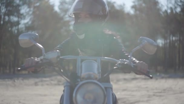 Portre güzel kız siyah kask giyen motosiklet üzerinde oturan uzağa bakıyor. Hobi, seyahat ve aktif yaşam tarzı. Bisikletçi dışarıda motosikletine biner. Eğlence ve motosiklet ile seyahat. Yumuşak ışık. — Stok video