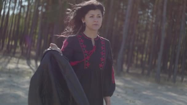 Jolie jeune femme caucasienne en belle robe longue noire et rouge debout dans la forêt de pins. Connexion avec la nature. Mouvement lent . — Video