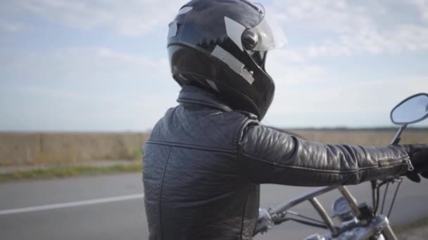 Flickan bär svart hjälm sitter på motorcykeln tittar bort på vägen. Hobby, resande och aktiv livsstil. Biker på sin motorcykel utomhus. Fritid och resa med motorcykel. Slow motion. — Stockvideo