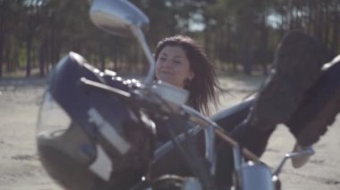 Siyah deri ceketli ve motosikletli pantolonlu beyaz ve güzel bir kadın. Hobi, seyahat ve aktif yaşam tarzı. Motosikletle eğlence ve seyahat.