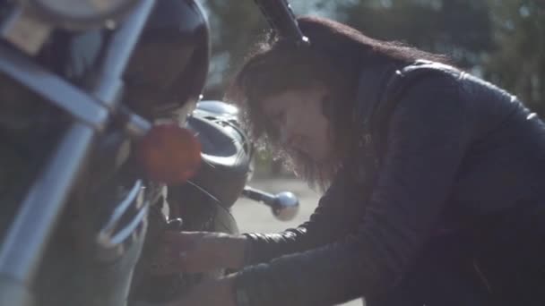 Ragazza caucasica fissare la sua moto o condizione di controllo in luce morbida primo piano. Hobby, viaggiare e stile di vita attivo. Biker donna con la sua moto all'aperto. Tempo libero e viaggi in moto . — Video Stock