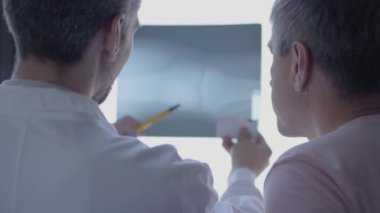 İki profesyonel doktor röntgeni kontrol ediyor, tartışıyorlar. Beyaz cüppeli adam laboratuvarda insan kemiklerinden bahsediyor. Tıp, teknoloji, sağlık ve insan kavramı, hastane.