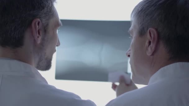 2人の技能医がX線写真をチェックし、議論する。白いローブをした男が 研究室で人間の骨について話してる医療、技術、ヘルスケアと人、病院の概念. — ストック動画