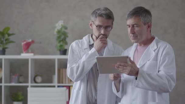 Dois médicos do sexo masculino a verificar informações no tablet, a discutir. Conceito de medicina, tecnologia, cuidados de saúde e pessoas, hospital. Nova instalação médica moderna totalmente funcional . — Vídeo de Stock