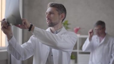 Modern kliniğin ofisinde röntgeni kontrol eden iki erkek doktor var. Beyaz cüppeli genç adam eski meslektaşına röntgen gösterip tavsiye ve onay istiyor. Yeni modern tam fonksiyonel tıbbi tesis.