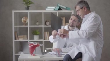 Modern kliniğin ofisinde röntgeni kontrol eden iki erkek doktor var. Erkekler fikir birliğine varır ve el sıkışırlar. Tıp kavramı, sağlık ve insanlar, hastane. Yeni modern tam fonksiyonel tıbbi tesis