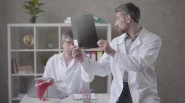Modern kliniğin ofisinde röntgeni kontrol eden iki erkek doktor var. Doktor cüppegenç adam tavsiye ve onay isteyen eski meslektaşına x-ray gösteren. Tıbbi tedavi kavramı