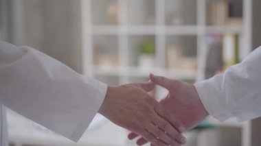 Doktorlar gibi beyaz önlüklü tanınmayan iki erkek elinin kendine güvenen dostça el sıkışması. Tıp kavramı, sağlık ve insanlar, hastane. Yeni modern tam fonksiyonel tıbbi tesis.