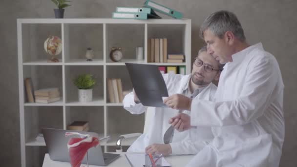 Zwei männliche Ärzte bei der Röntgenuntersuchung im Büro einer modernen Klinik. Konzept der Medizin, Gesundheitsfürsorge und Menschen, Krankenhaus. neue moderne, voll funktionsfähige medizinische Einrichtung. — Stockvideo