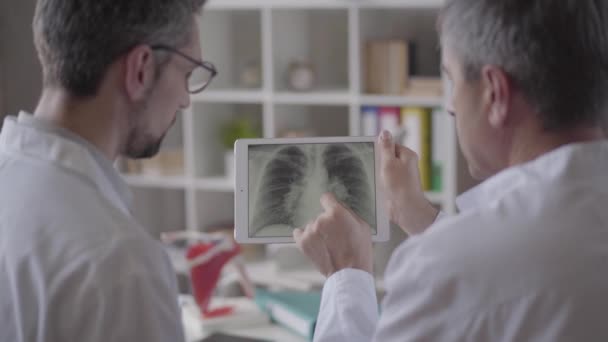 Dos médicos varones experimentados revisando la radiografía de los pulmones en la tableta, discutiendo. Concepto de medicina, salud y personas, hospital. Nueva instalación médica moderna totalmente funcional . — Vídeos de Stock