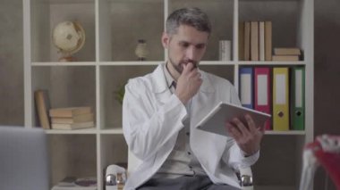 Beyaz cüppe yakışıklı düşünceli adam portresi akciğerx-ray resmi ile tablet gösteren kamera bakıyor. Modern özel klinikte usta doktor. Yeni tam fonksiyonel tıbbi tesis.