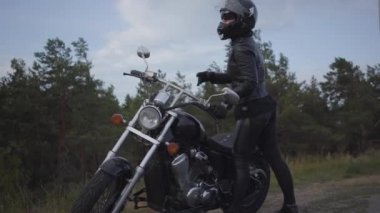 Siyah deri ceket ve kask klasik bir motosiklet sürme Beceri kafkas kadın. Kız yol kenarında motosiklet yanında duran kask kaldırır. Hobi, seyahat ve aktif yaşam tarzı.