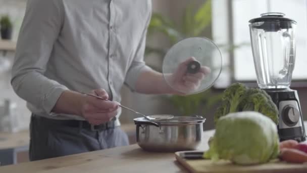 Knappe goed uitziende man in het shirt koken soep in de keuken. Concept van gezond eten, thuis koken. De man koken eten na het werk — Stockvideo