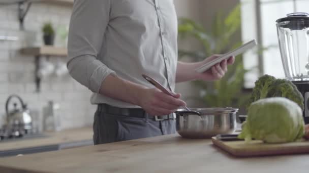 在厨房的平板电脑上，在衬衫上煮汤检查食谱的无法辨认的人。健康食品的概念，家庭烹饪。下班后做饭的家伙 — 图库视频影像