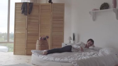 Karısı elbiselerini değiştirirken, romantik tarih veya parti için elbise seçerken genç adam yatakta yatıyordu. Mutlu genç ailenin eğlencesi.