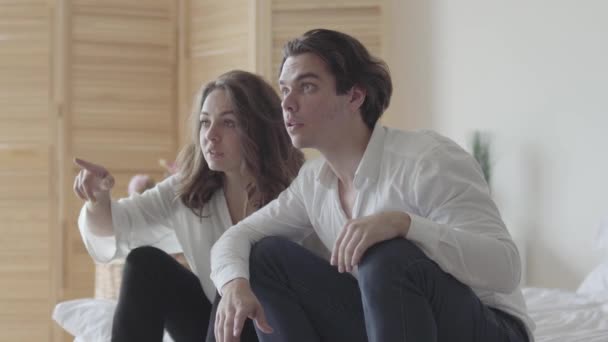 Un jeune homme et une jeune femme émotionnels regardant le football ou le baseball assis sur le lit. La relation entre l'homme et la femme. Les amateurs de football à la maison célèbrent ensemble un objectif — Video