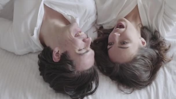 Сверху кадры счастливая молодая пара, лежащая на кровати и разговаривающая крупным планом. Вид сверху расслабляющий мужчина и женщина . — стоковое видео