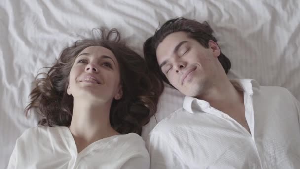 Carino uomo e donna che cadono sul letto e si guardano con amore. Giovane coppia sdraiata sul letto. Una tenera relazione romantica. Rallentatore . — Video Stock