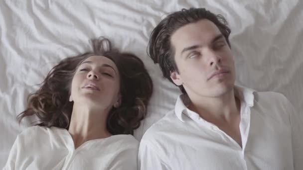 Bărbat și femeie fericiți căzând pe pat și uitându-se unul la celălalt cu dragoste. Cuplu tânăr întins în pat. Relaţie romantică delicată. Slow motion . — Videoclip de stoc