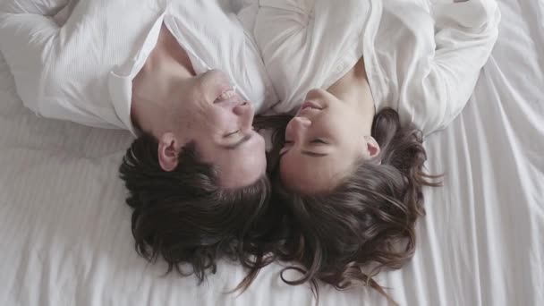 Overhead disparó feliz pareja joven acostada en la cama hablando de cerca. Vista superior relajante hombre y mujer. Movimiento lento . — Vídeo de stock