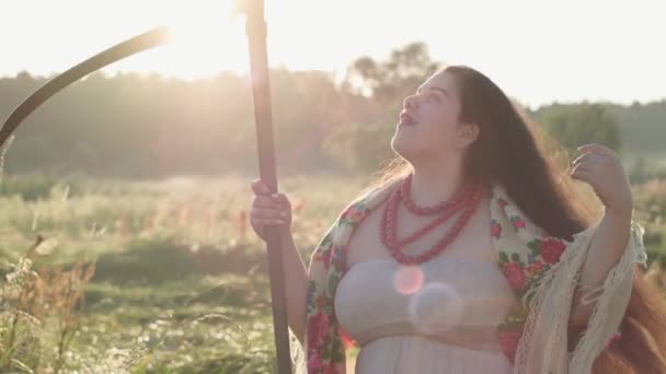 Beautiful overweight woman with a scythe in sunlight on the green summer field. Beautiful landscape. Folklore, traditions concept. Work in the field. Real rural woman. — Stock Video