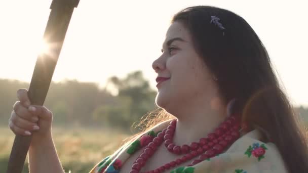 Close-up portrait cute overweight woman holding a scythe on the green summer field in sunlight. Beautiful landscape. Folklore, traditions concept. Work in the field. Lens flares. Real rural woman. — Stock Video