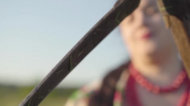 Kilolu kadın yeşil yaz alanında biçme başlamak için hazırlanıyor tırpan keskinleştirme. Çiftçi tırher'ı öğütücüyle bileyor. Folklor, gelenekler kavramı. Sahada çalışma