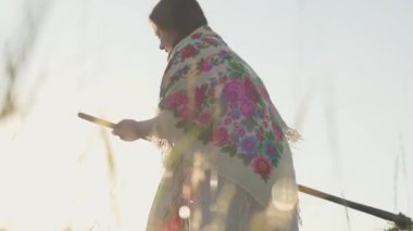 Sevimli tombul kadın yeşil yaz alanında tırp ile çim biçme. Folklor, gelenekler. Sahada çalış. Kadın çiftçi çiftliğinde gün doğumu arka plan üzerinde çalışıyor. Gerçek kırsal kadın.