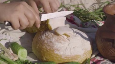 Beyaz ekmeğin somununu kesen genç bir kadının yakın elleri. Sağlıklı gıda, Ukrayna geleneksel mutfağı, ülke yaşam tarzı. Sağlıklı yiyecekler. Gerçek kırsal bir kadın. Kırsal kesimde öğle yemeği molası.
