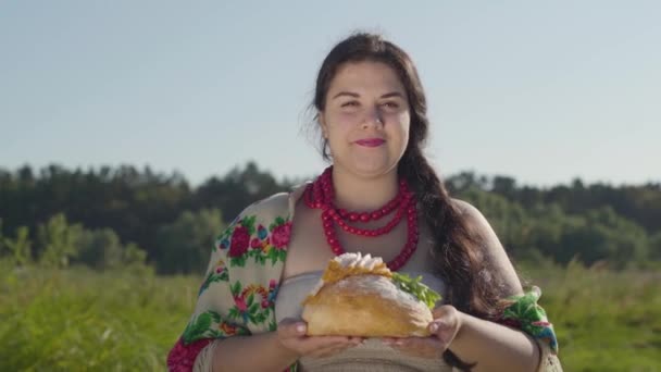 Porträt einer süßen dicken Frau, die Schmalz auf dem Laib Weißbrot anbietet und lächelnd in die Kamera schaut. Gastfreundschaftskonzept. Echte Landfrau. — Stockvideo