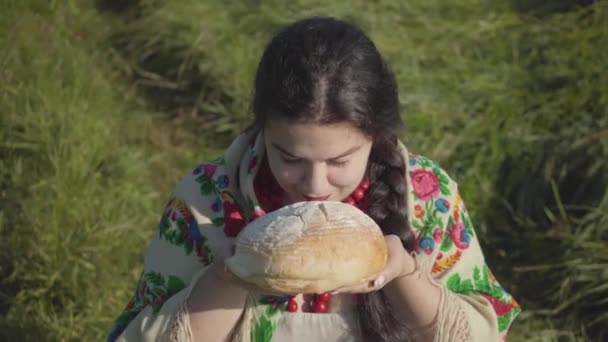 Retrato de una linda mujer con sobrepeso sentada en la hierba oliendo sabroso pan que se prepara para comer. Concepto de tradiciones. Estilo de vida rural. Una verdadera mujer rural. Almuerzo en el campo . — Vídeo de stock