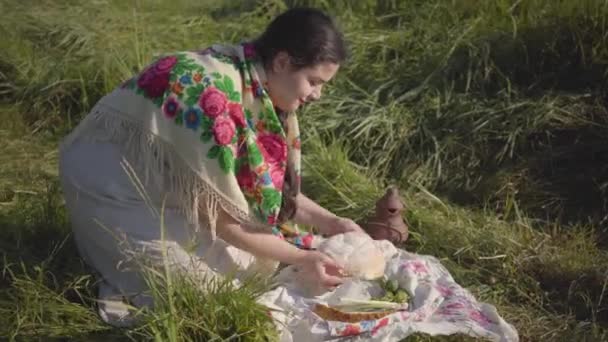 Beautifu mujer con sobrepeso sentado en la hierba silvestre con la hogaza de pan y tarro de barro preparándose para comer. Concepto de tradiciones, conexión con la naturaleza. Estilo de vida — Vídeo de stock