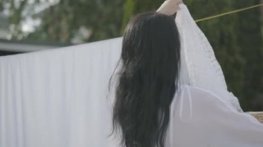 Uzun saçlı çekici kadının geri görünümü bir çamaşır ipi açık havada beyaz giysiler asılı. Yıkanıyor. Çamaşır yıkadan bir kız. Sürdürülebilirlik kavramı, doğa ve saflık ve yıkandıktan sonra derin temiz.