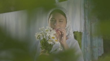 Kafasında beyaz şal ile Çekici yaşlı kadın çamaşır ipi açık havada papatya yaprakları kapalı gözyaşları. Yıkanıyor. Pozitif kaygısız ev hanımı çamaşır yıkıyorum. Ağaç brunch arkasından Çekim