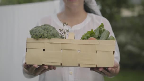 Femme méconnaissable en robe blanche avec un châle sur la tête tenant le panier avec des légumes à l'extérieur. Femme au foyer positive faisant des travaux ménagers. Style de vie rural sain — Video