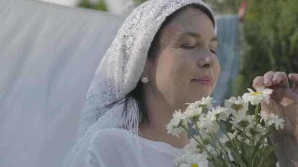 Senior Kvinna med vit sjal på huvudet sniffa prästkragar nära klädstreck utomhus. Gick. Positiv bekymmerslös hemmafru gör tvätt. — Stockvideo